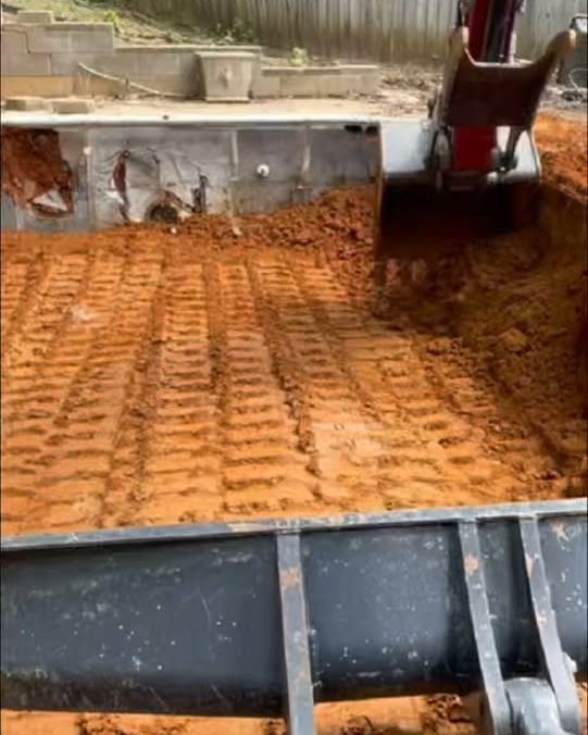 Excavator bucket over a freshly graded red dirt pad